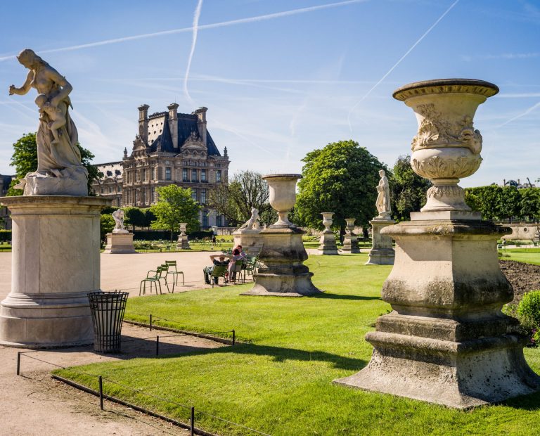 View of the Tuileries garden in Paris by a sunny morning with the statue of Medea and a carved vase in the foreground and the Flore pavilion of the Louvre palace in the background